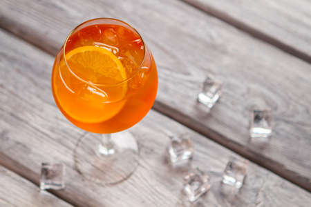 Orange cocktail in wineglass with Ice cubes on wooden background.の写真素材