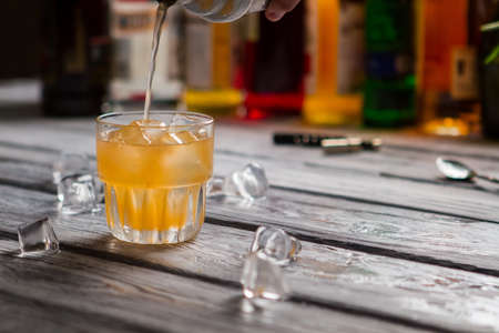 Orange liquid pours into glass and Melting ice on wooden surface.の写真素材