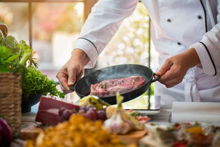 Raw meat on black pan. Man's hands hold frying pan. Professional cook in the kitchen. Best recipe of...