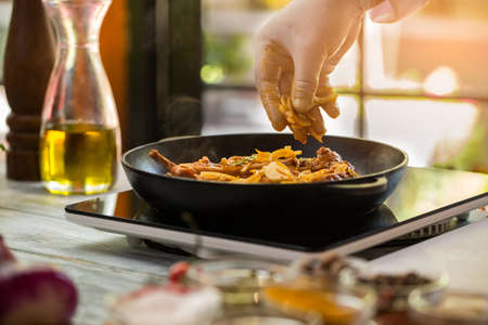 Meat on a pan. Hand holds onion pieces. Recipe of pork from chef. Preparation of meal in cafe.の写真素材