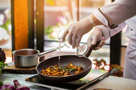 Liquid pours onto mushrooms. Hand holding glass over pan. Chanterelles fried in wine. Chef tries new recipe.の写真素材