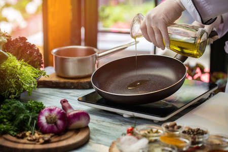 Jug pours liquid on pan. Green lettuce and purple onion. Frying pan is warming up. Need some olive...