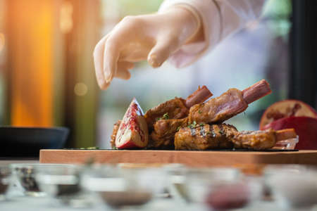 Hand near board with meat. Herbs and piece of pomegranate. Special recipe of veal ribs. Tasty and aromatic dish.の写真素材
