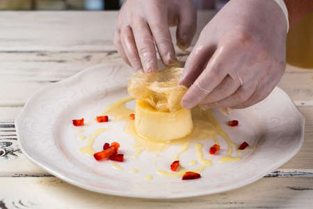 Small cake on white plate. Hands in gloves touch dessert. Chef is decorating creme caramel. Fresh...