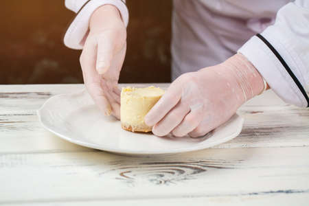 Hands in gloves touch dessert. Plate with small cake. Pastry chef prepared cheesecake. Best sweet dish in menu.の写真素材