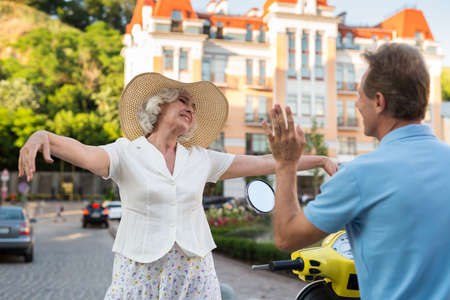 Adult man waves his hand. Smiling lady in a hat. We finally met. Nice surprise during travel.の写真素材