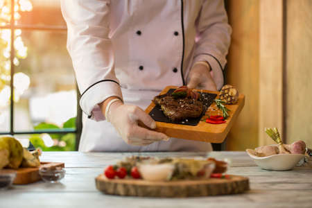 Hands hold board with meat. Rosemary and chili peppers. Appetizing ribeye steak. Skills of professional cook.の写真素材