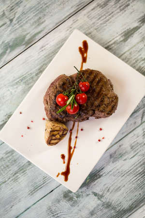 Cooked meat on plate. Tomatoes and roasted garlic. Tenderloin steak served with thyme. Lunch on gray wooden table.の写真素材