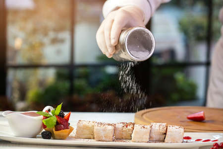 White powder falls on dessert. Hand in glove holds jar. Berry rolls with powdered sugar. Sweet dish...