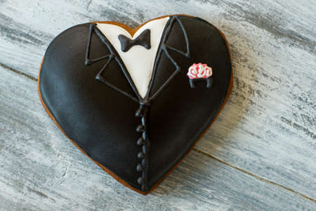 Heart shaped tuxedo cookie. Biscuit with black icing. Small surprise for groom. Special taste of holiday.の写真素材