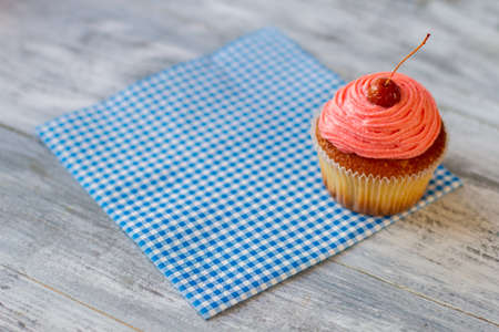 Frosted cupcake on a napkin. Dessert with cherry on top. Pastry served at the cafe. Sweet treat for visitors.の写真素材