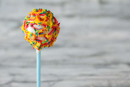 Dessert on stick. White glaze and sprinkles. Try the sweet masterpiece. Candy with soft filling.