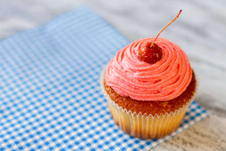 Cupcake on checkered napkin. Pink icing and cherry. Sweet treat in local cafe. Dessert with new flavor.の写真素材