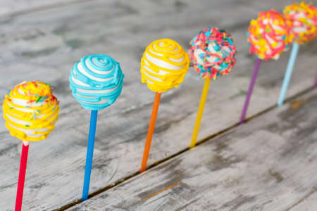 Row of cake lollipops. Candies on gray wooden background. Bright colored sweets with filling. Make desserts for children.の写真素材
