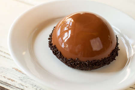 Brown half sphere cake. Dessert with smooth surface. Chocolate mousse and mirror glaze. Tasty sweet dish in cafeteria.の写真素材