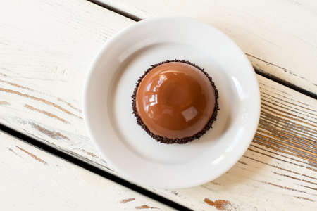 Small glazed cake on plate. Top view of brown dessert. Mirror glaze and chocolate mousse. Freshly made dish in cafeteria.の写真素材