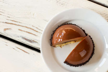 Dessert with mirror icing. White plate with brown cake. Chocolate mousse and soft dough. Freshly made sweet treat.の写真素材