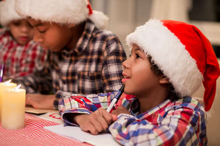 Children writing letter to Santa. Afro kids write Christmas letter. Making a Christmas wish list. Think about best presents.の写真素材