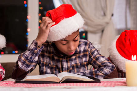Little Santa reads a book. Boy reading book on Christmas. Reading Christmas stories beside window. Kid's leisure time on holidays.の写真素材