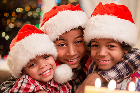 Three kids in Christmas hats. Smiling afro boys on Christmas. Three happy brothers on holidays. Christmas evening at family house.の写真素材