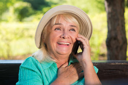 Smiling mature woman with phone. Happy lady wearing a hat. Congratulations from grandson. Priceless...