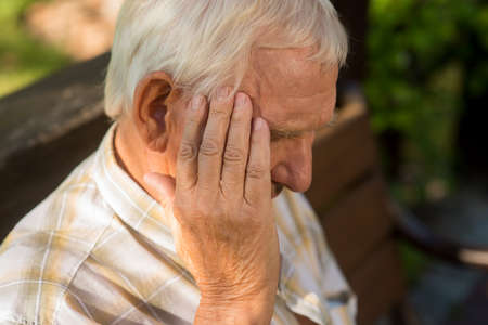 Senior man holds his head. Old person has headache. Pain is getting stronger. What a stressful day.の写真素材