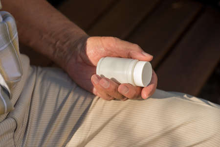 Male hand with pill bottle. White medicine container. Must use painkillers. Doctor prescribed a drug.の写真素材