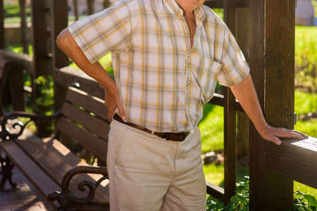 Elderly male has backache. Man leans on wooden fence. Problems with spine. Pain from herniated disk.