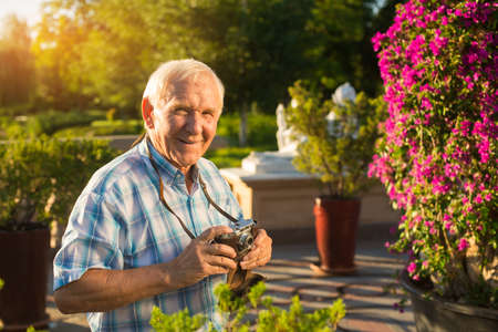 Man smiling and holding camera. Old male outdoors. Active leisure after retirement. Never get bored.の写真素材