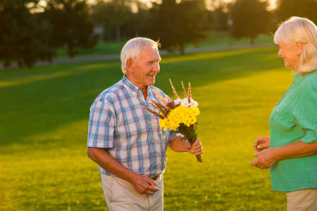 Smiling senior man with bouquet. Couple on meadow background. Surprise for beloved wife. Your favorite flowers.の写真素材
