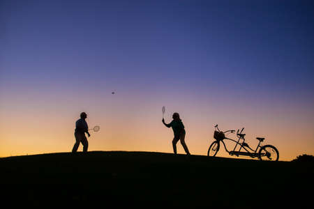 Couple is playing badminton. People on evening sky background. Play until you win. Test of endurance.の写真素材