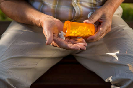 Elderly hand holds white pills. Orange medicine container. Drug against heartache. Follow the...