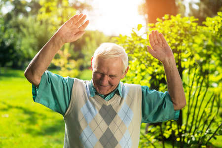 Man smiling and looking down. Senior male with raised arms. You got me. Cunning plan didn't work.