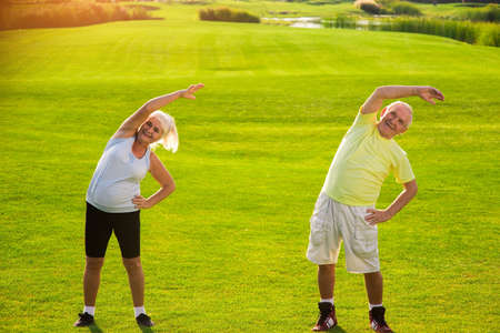 Elderly couple doing exercise. Man with woman on meadow. Gymnastics for health. Good day for a...