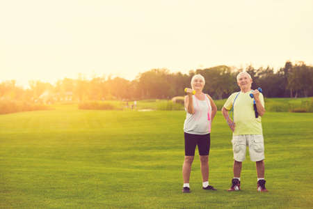 Couple with dumbbells smiling. Senior people standing outdoor. New training program for pensioners. Life and sports.の写真素材
