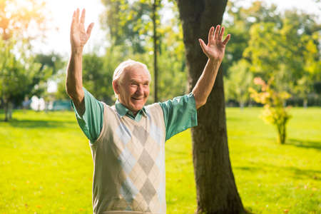 Senior male with raised arms. Smiling elderly man outdoor. Grandpa meets grandson. Heart in joy.