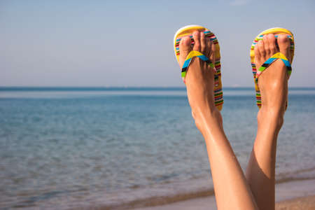 Woman's legs and sea. Feet wearing flip flops. Leave bustle and problems behind. The dream vacation.の写真素材