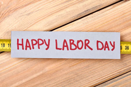 Happy Labour Day greeting paper. Tape measure on wooden background. Handmade congratulation card.の写真素材