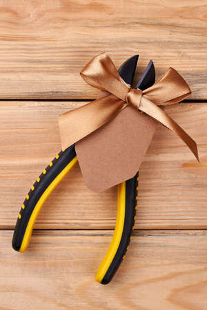 Pliers decorated with ribbon bow. Tool on wooden background. Gift for true man.の写真素材
