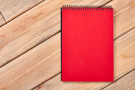 Red notebook on wooden surface. Spiral paper notepad on table. Space for doodling.の写真素材