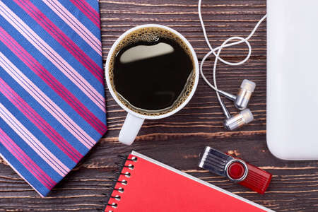 Coffee, flash drive and earphones. Notepad and necktie on wood. Tasty beginning of working day.の写真素材