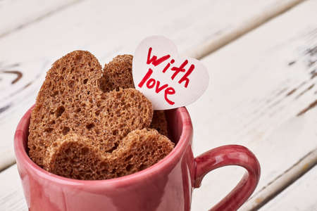 Greeting card and bread hearts. Pink cup on wooden surface. Joy of feeling love.の写真素材