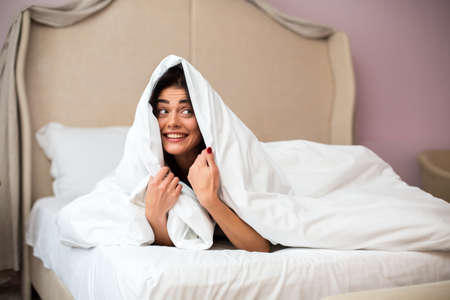 Lady hiding under a blanket. Smiling woman indoors. Girl in cheerful mood.の写真素材