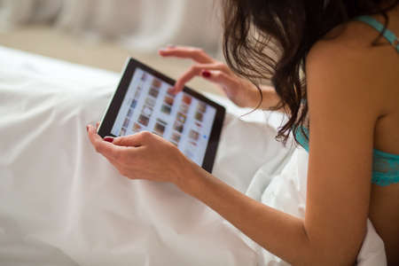 Female in bed with tablet. Ladys hand holding gadget. Ordering goods through site.の写真素材