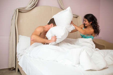 Pillow fight of couple. Woman laughing indoors. Win a fair fight.の写真素材