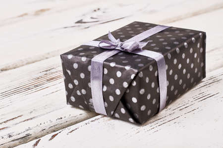 Present package and violet ribbon. Spotty gift box on wood. Gift wrapping tutorial.の写真素材
