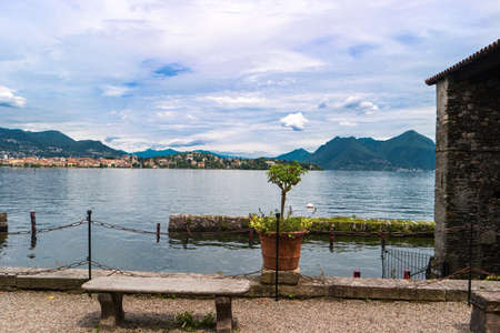 Nature and town buildings. Stone bench near water. Picturesque view of Maggiore lake.の写真素材