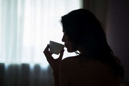 Lady holding cup in darkness. Young woman indoors. Day starts from hot beverage.の写真素材