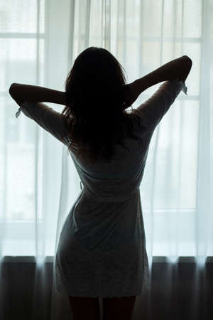 Woman standing near window. Lady wearing a nightie. When beauty wakes up.の写真素材