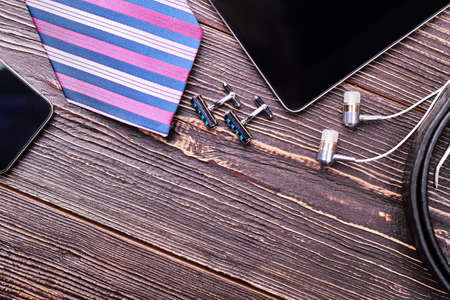 Cufflinks and striped necktie. Earphones and tablet on wood. Accessories of a successful man.